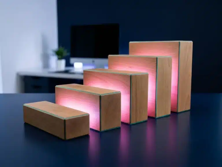 Fünf geometrische Holzblöcke in aufsteigender Treppenstufen-Anordnung mit rosa und magenta Akzentbeleuchtung auf dunkler Oberfläche