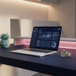 Moderner Arbeitsplatz mit weißem Laptop, analoger Armbanduhr und Pflanze auf dunkler Oberfläche bei rosa Akzentbeleuchtung