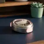 Moderne Stoppuhr mit rosa Akzenten auf dunkelblauem Schreibtisch neben türkiser Pflanze bei warmem Licht