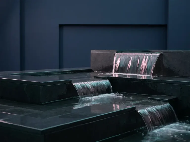 Eleganter Wasserfall fließt über dunkle Steinstufen mit rosa Beleuchtung in minimalistischer Architektur