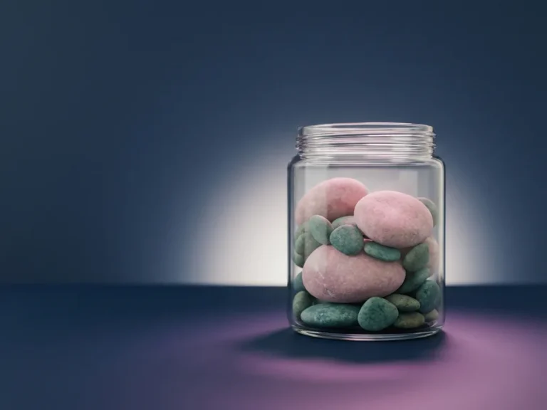 Glasgefäß mit verschieden großen Steinen in Rosa- und Türkistönen auf dunkelblauem Untergrund, minimalistisches Studio-Stillleben.