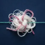 Weißes Fadenbündel mit Knoten, durchzogen von rosa und magentafarbenen Fasern, neben einem geraden türkisen Faden auf dunkelblauem Untergrund.